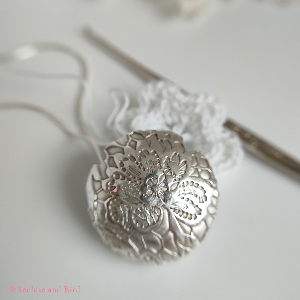 close up of a round lentil bead made of silver resting on a crochet hook and small Irish crocheted rose