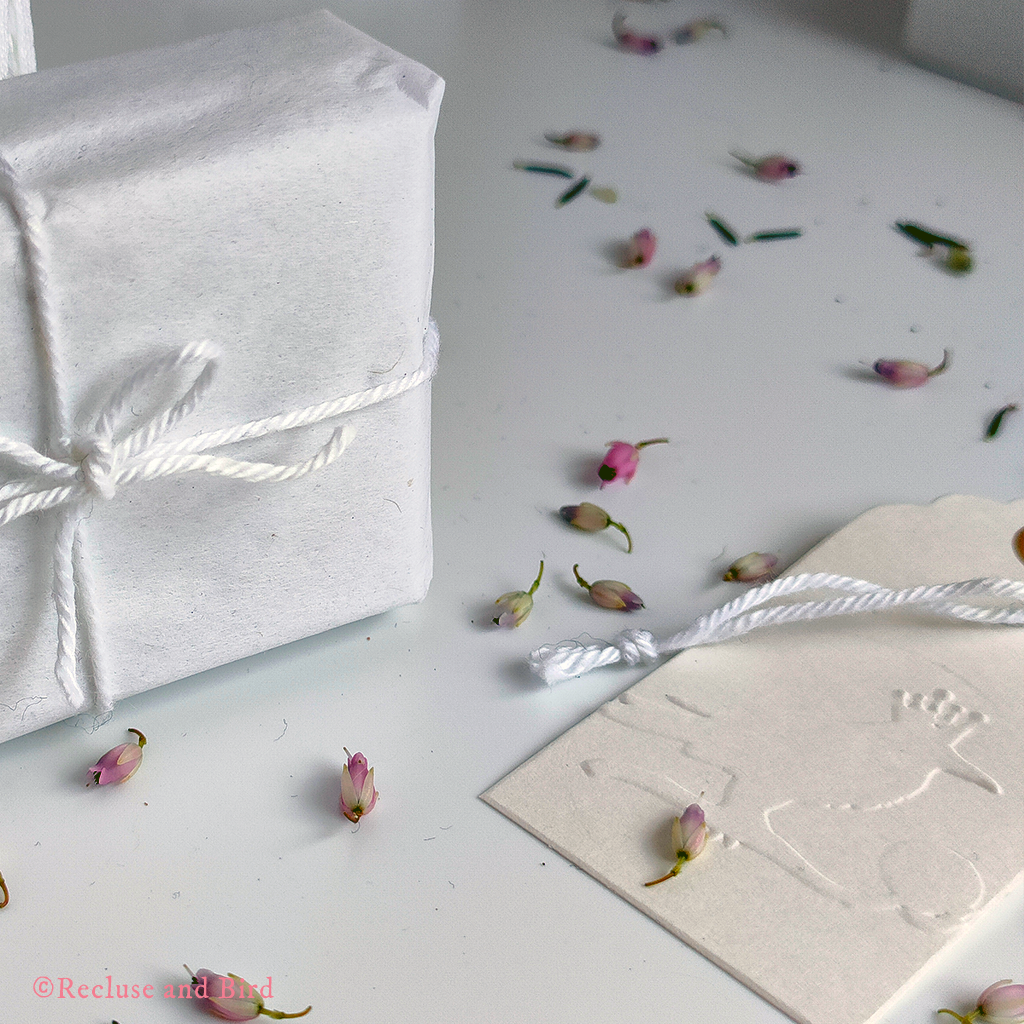 photo of a small jewellery box wrapped in white paper with brow string and a little white kraft tag with the logo of Recluse and Bird embossed in it